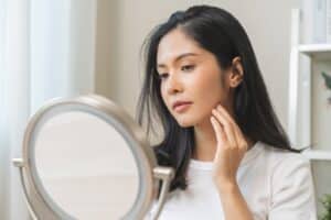 A woman looking in the mirror and wondering how often she needs a skin exam.