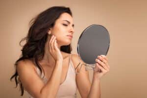 A woman looking in the mirror at her acne during summer